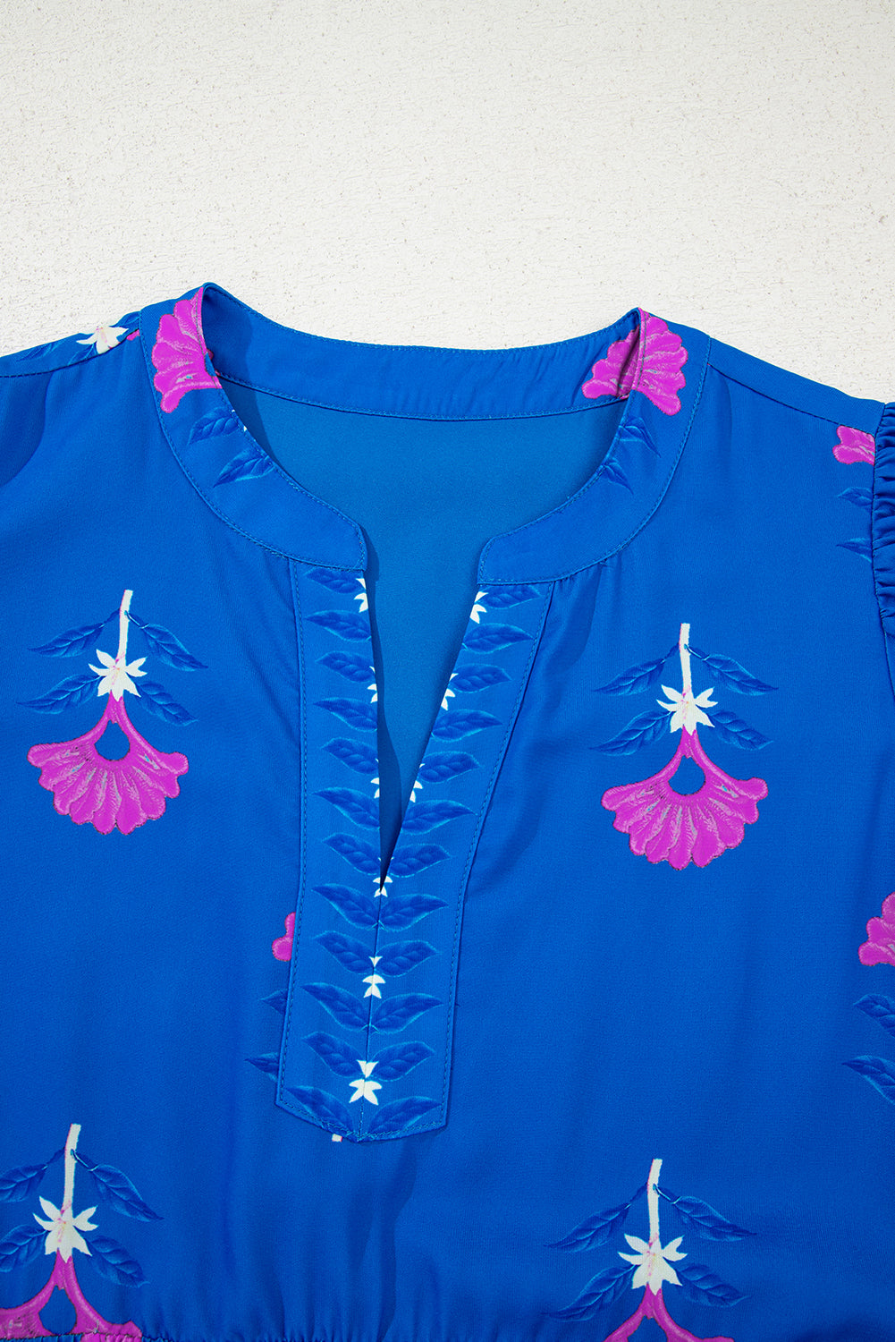 Blue top with pink and white floral embroidery on a light gray background