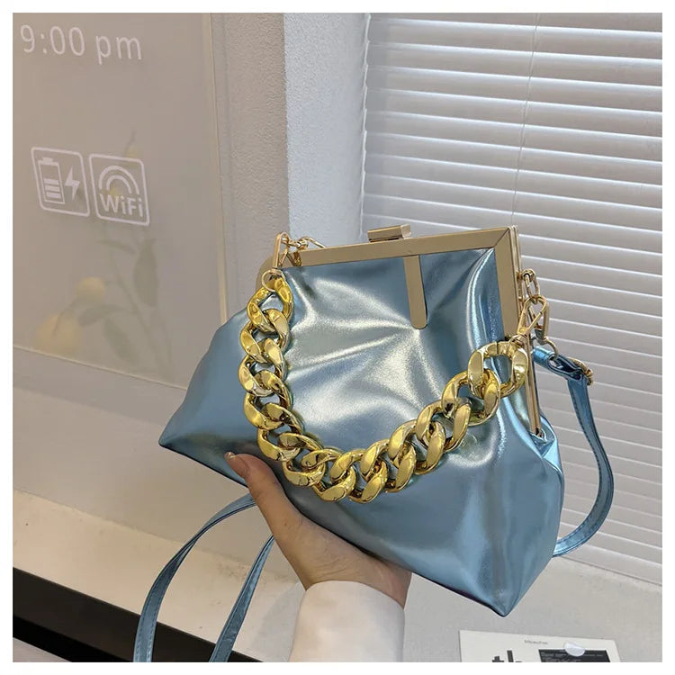 Carauana UNIU Aurora Clutch with gold chain detail held by a hand in an indoor setting.