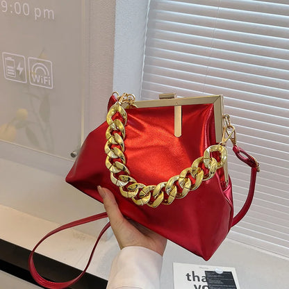 Carauana UNIU Aurora Clutch Red handbag with gold chain handle held by a hand, indoor setting.