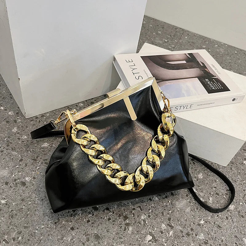 Black Carauana UNIU Aurora Clutch handbag with gold chain detail on a concrete surface