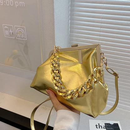 Gold Carauana UNIU Aurora Clutch handbag with chain detail held by a person in an indoor setting.