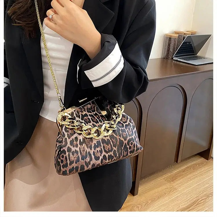 Person holding a Carauana_UNIU_Leopard_Clutch with gold chain detail indoors.