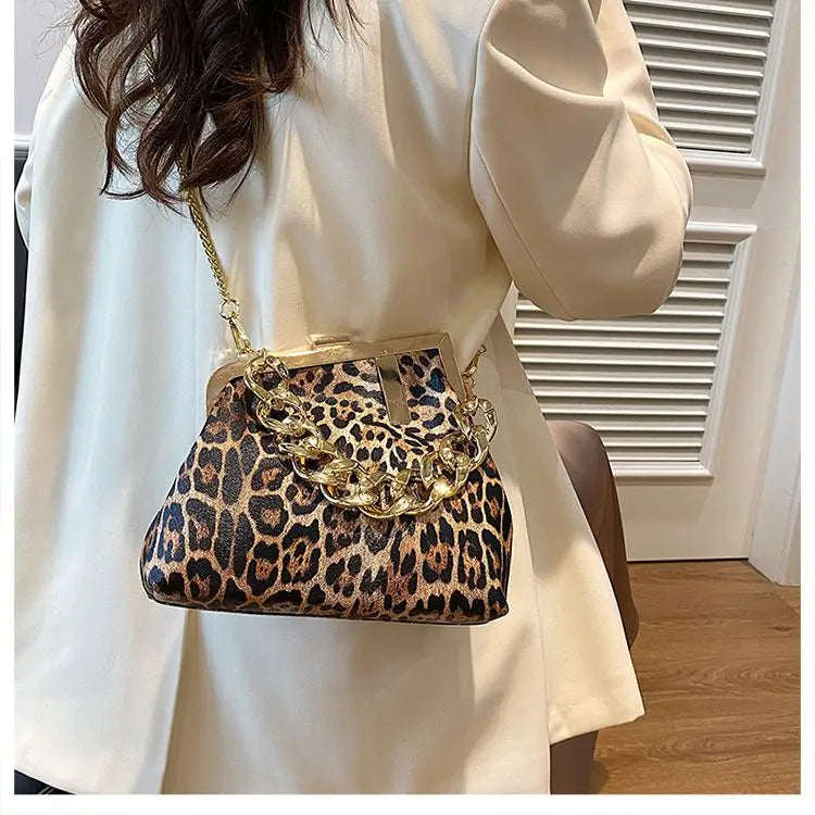 Person holding aCarauana UNIU Leopard Clutch handbag with gold accents indoors.