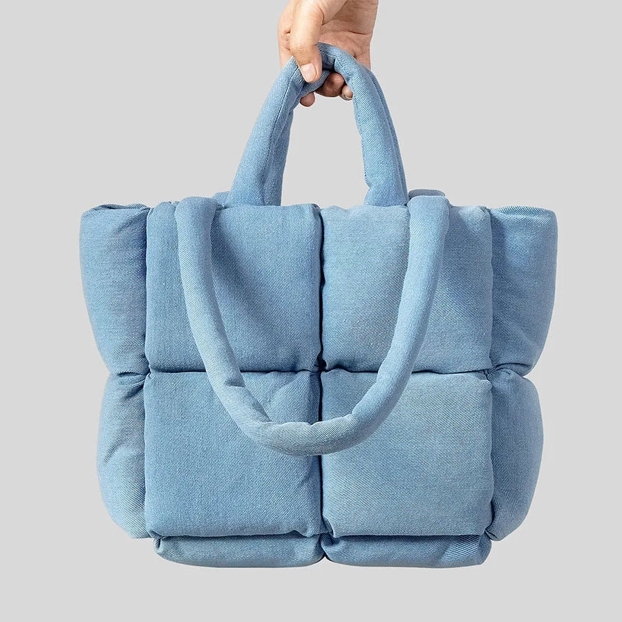 Blue textured tote bag held by a hand against a light gray background